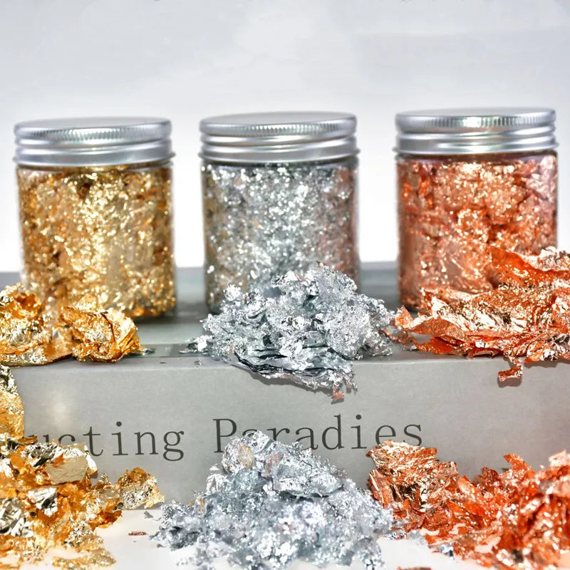 Various metallic foil flakes in gold, silver, and copper colors displayed in glass jars.