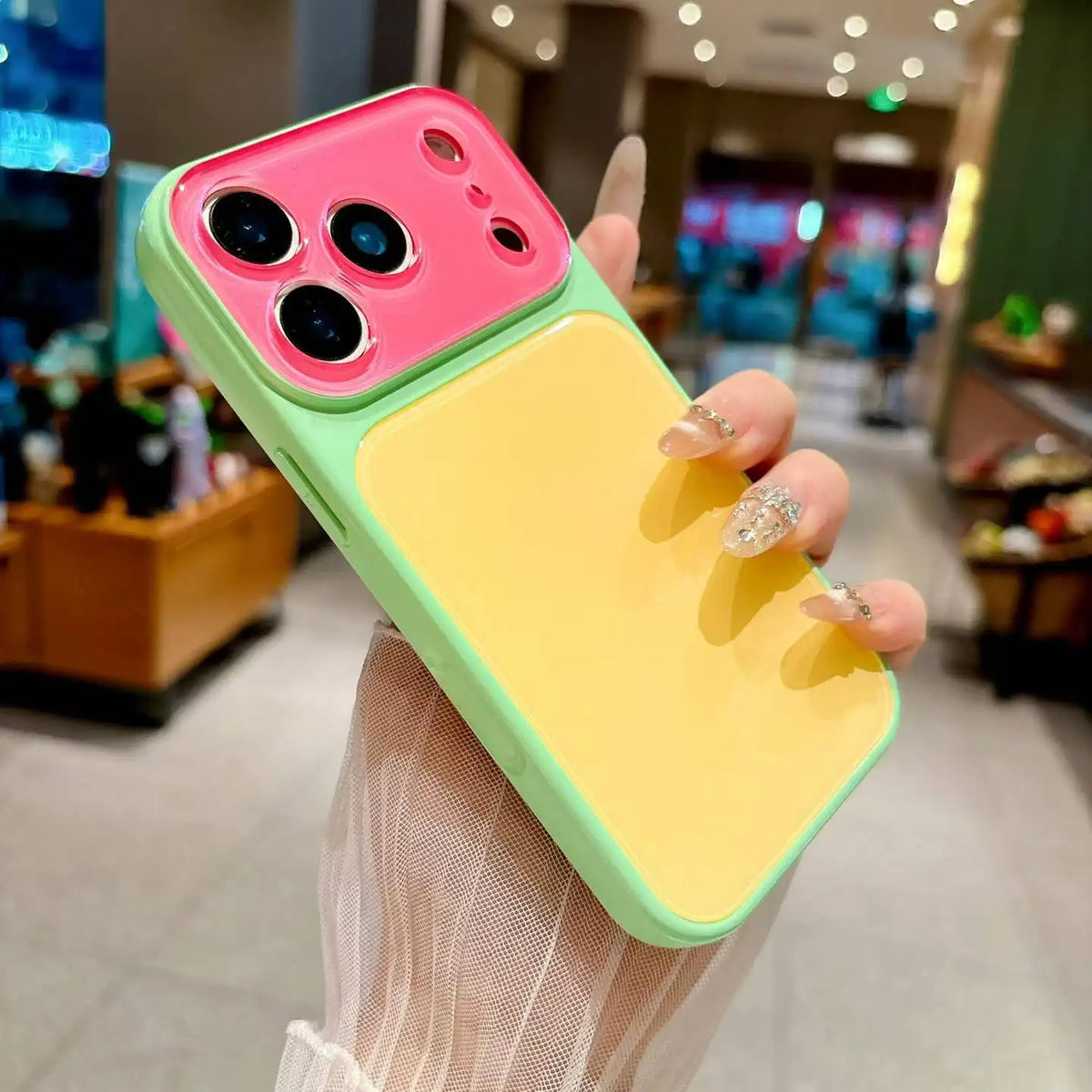 A hand holds a color blocking phone case with a pink back and yellow front, displaying the large camera window.