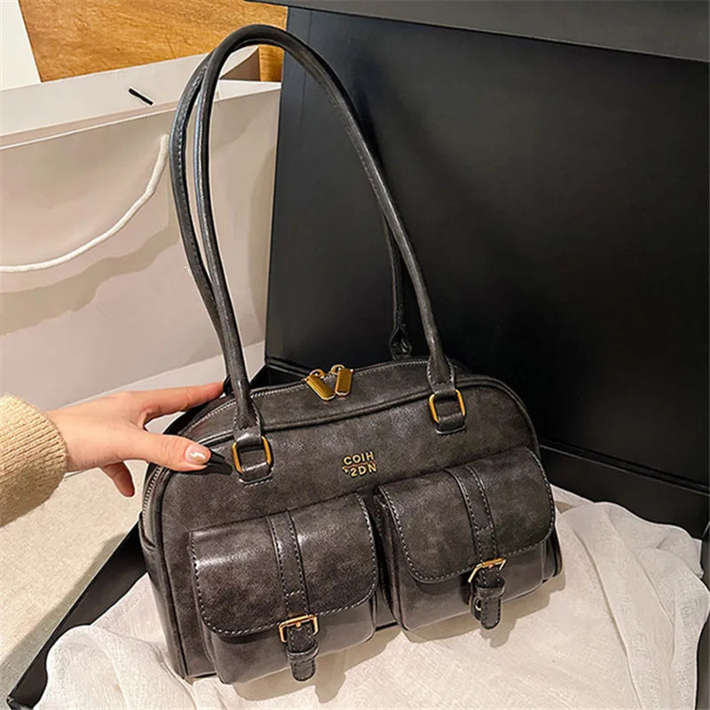 Dunkelgrabe Lederhandtasche mit Gold-Hardware vor schwarzem Hintergrund