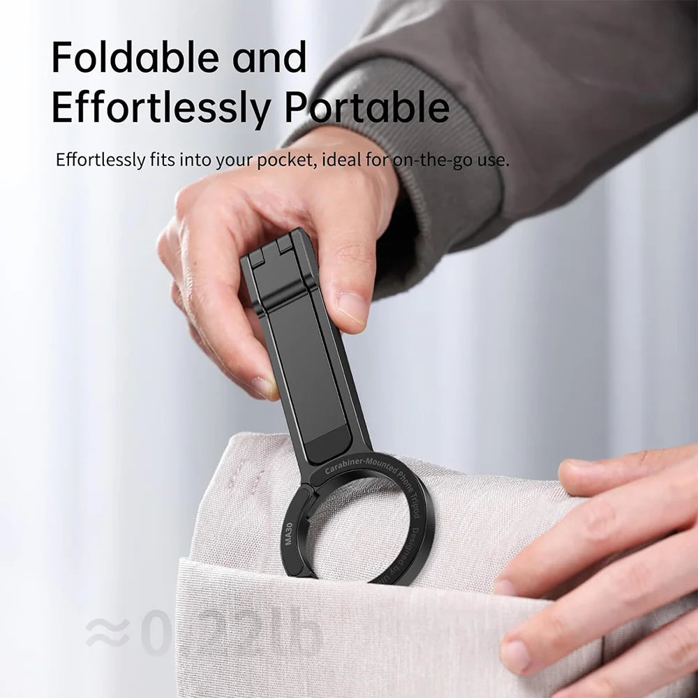 A hand is holding a black magnetic phone tripod with a carabiner clip, demonstrating its portable design.