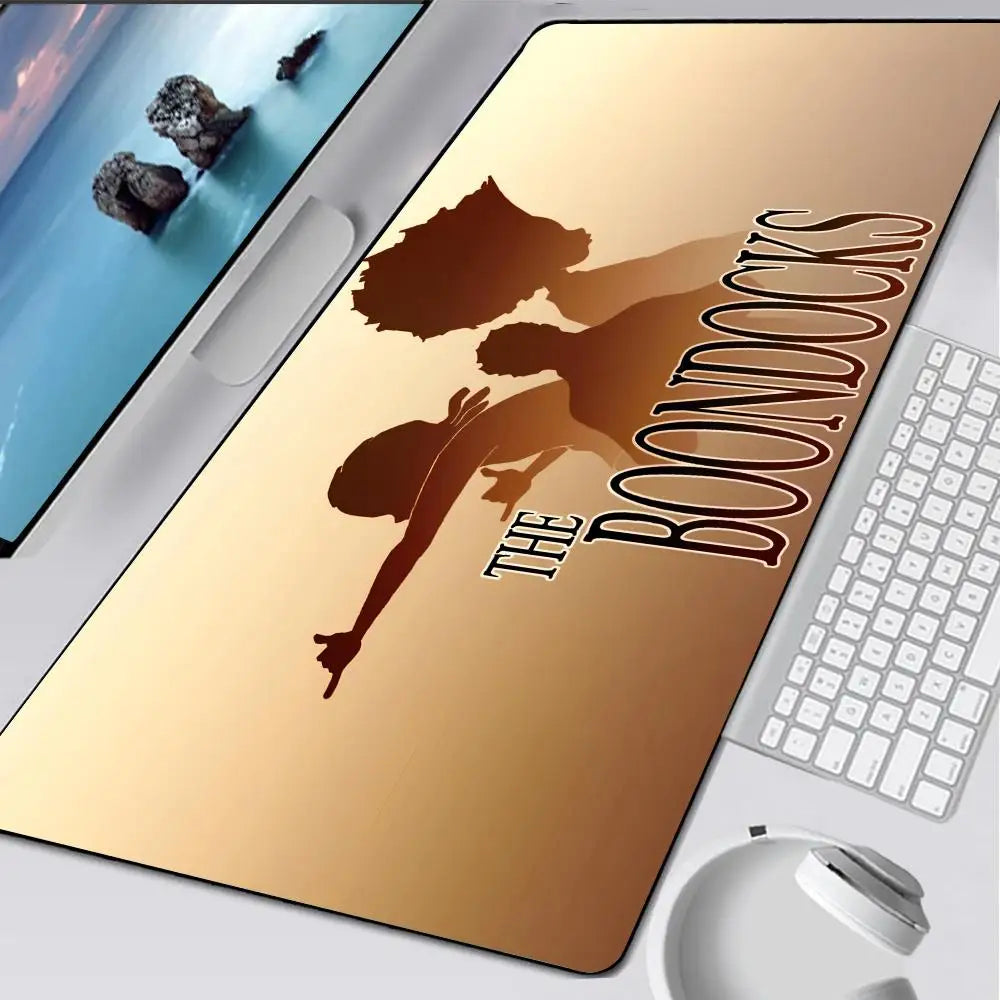 A close-up of a large, tan gaming mouse pad with the title The Boondocks printed on it, next to a laptop and a mouse.