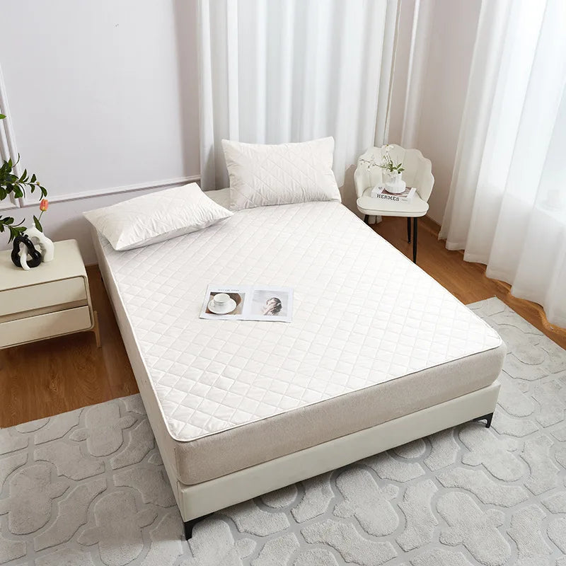 A white waterproof mattress protector with elastic straps is displayed on a bed, featuring a quilted surface.