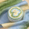 A roll of colorful gradient cake yarn in green and yellow tones displayed on a blue knitted fabric.