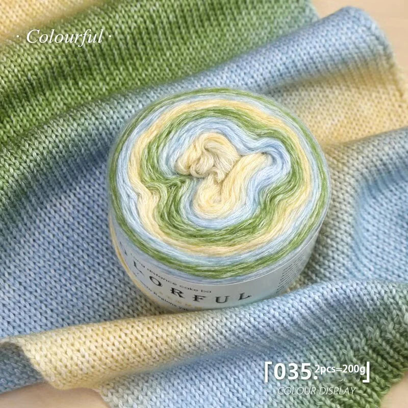 A roll of colorful gradient cake yarn in green and yellow tones displayed on a blue knitted fabric.