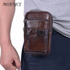 A brown genuine cowhide leather crossbody sling bag is shown being held by a person against a gray shirt and dark pants.