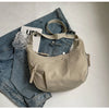 A beige lightweight nylon crossbody bag resting on a pair of blue denim jeans.