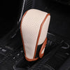 A beige and brown leather gear shift knob cover is shown resting on a black car interior surface.
