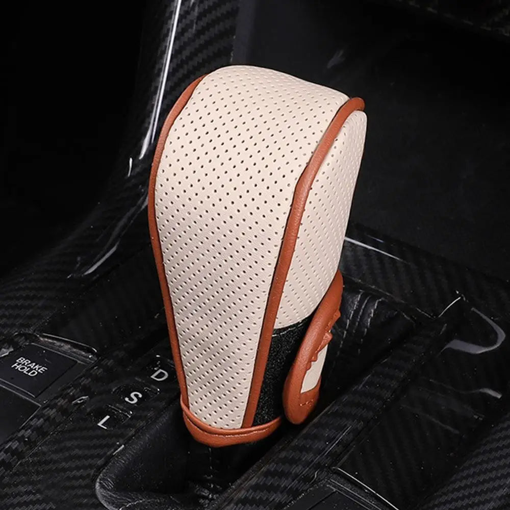 A beige and brown leather gear shift knob cover is shown resting on a black car interior surface.