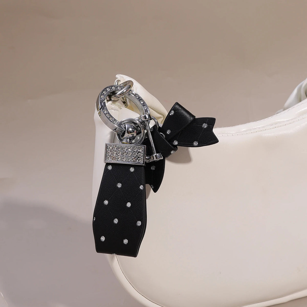 A black PU leather bow keychain with an O-shaped silver buckle attached to a white leather bag.