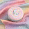 A roll of soft, colorful gradient yarn in pink and purple tones displayed on a pink knitted fabric.