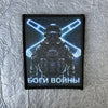 A black tactical patch featuring a glowing blue skull design with crossed lightsabers and the text БОГИ ВОЙНЫ.