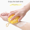 A hand is squeezing a yellow, porous bath sponge ball onto skin for bathing.
