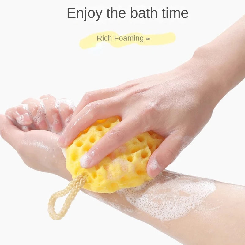 A hand is squeezing a yellow, porous bath sponge ball onto skin for bathing.