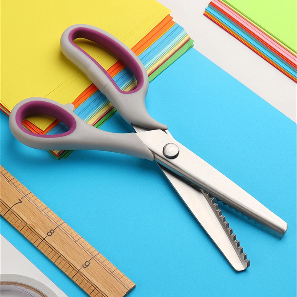 A pair of silver professional pinking shears lying on a blue surface next to colored paper and a wooden ruler.