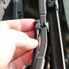 A hand is holding a black windshield washer nozzle assembly for a car, showing the connection point.