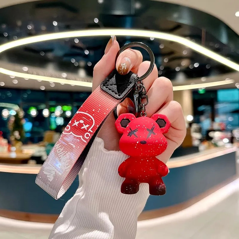 A hand holds a red bear-shaped keychain attached to a leather key case.