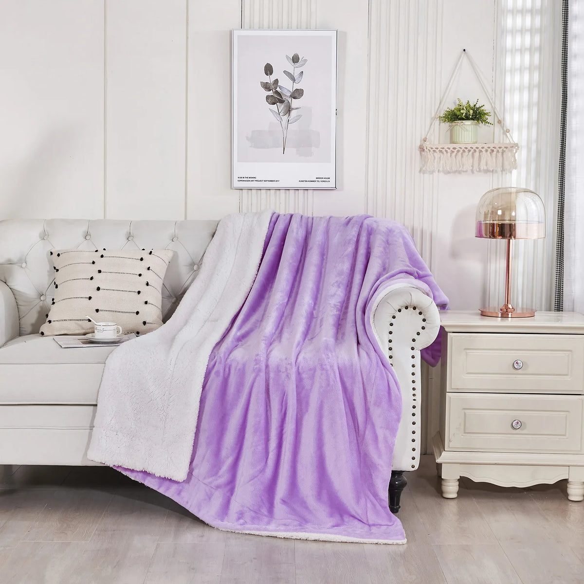Manta de sherpa morada y muy gruesa colgada sobre un sillón blanco en una habitación luminosa.