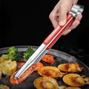 A hand holds a pair of stainless steel BBQ tongs used for grilling and serving seafood on a dark pan.