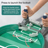A hand is pressing a handle button on a gray soccer game board to launch a ball into a goal.