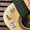 Close-up of a guitar body featuring stickers of golden retrievers and the text golden mom
