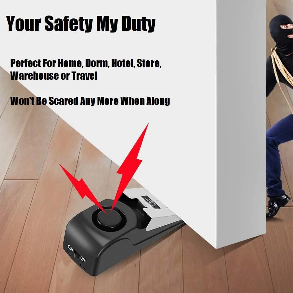 A black portable door stopper alarm with a wedge design is shown on a wooden floor.