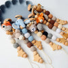 A collection of wooden pacifier clips featuring various crochet beads in natural and muted colors.