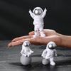 A pair of handcrafted astronaut figurines, one standing on a hand and another resting on a sphere.