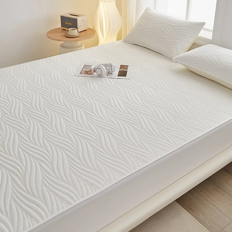 A white fitted mattress protector with a subtle wavy texture is displayed on a bed.