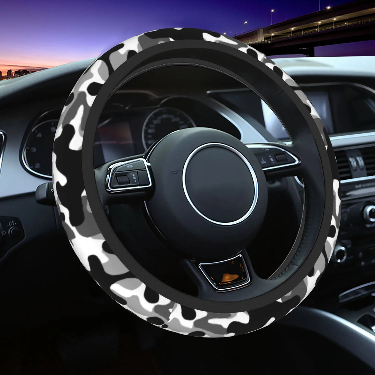 A black steering wheel covered with a white and gray camouflage pattern in a car interior.