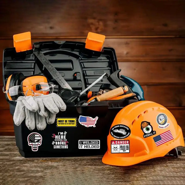 An open black toolbox shows various tools and an orange hard hat, with a yellow glove and a hard hat sticker pack nearby.