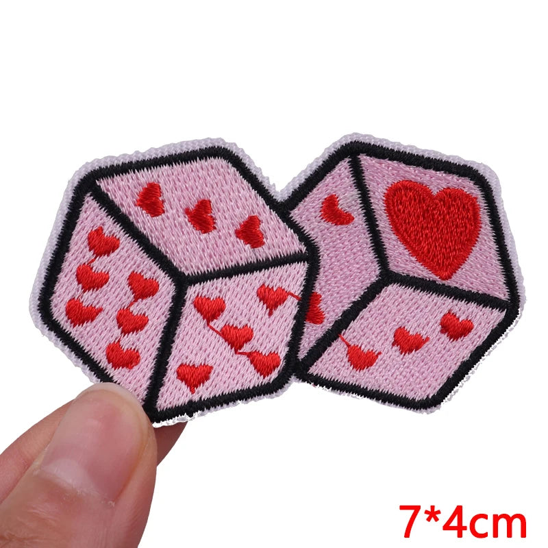 A set of pink and black embroidered dice featuring red hearts, shown being held.