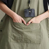 A person's hands are placing a leather pouch into the pocket of a sage green waterproof apron.
