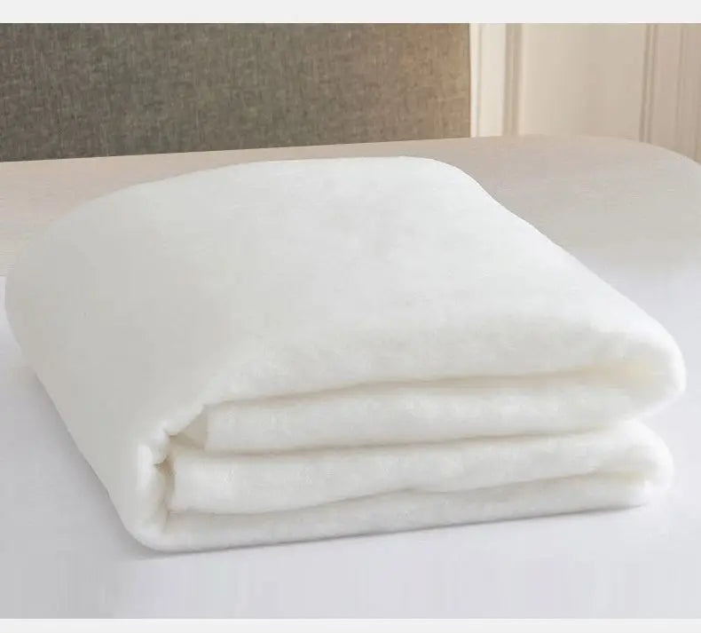 White folded quilt or blanket showing soft, fluffy texture on a white surface.