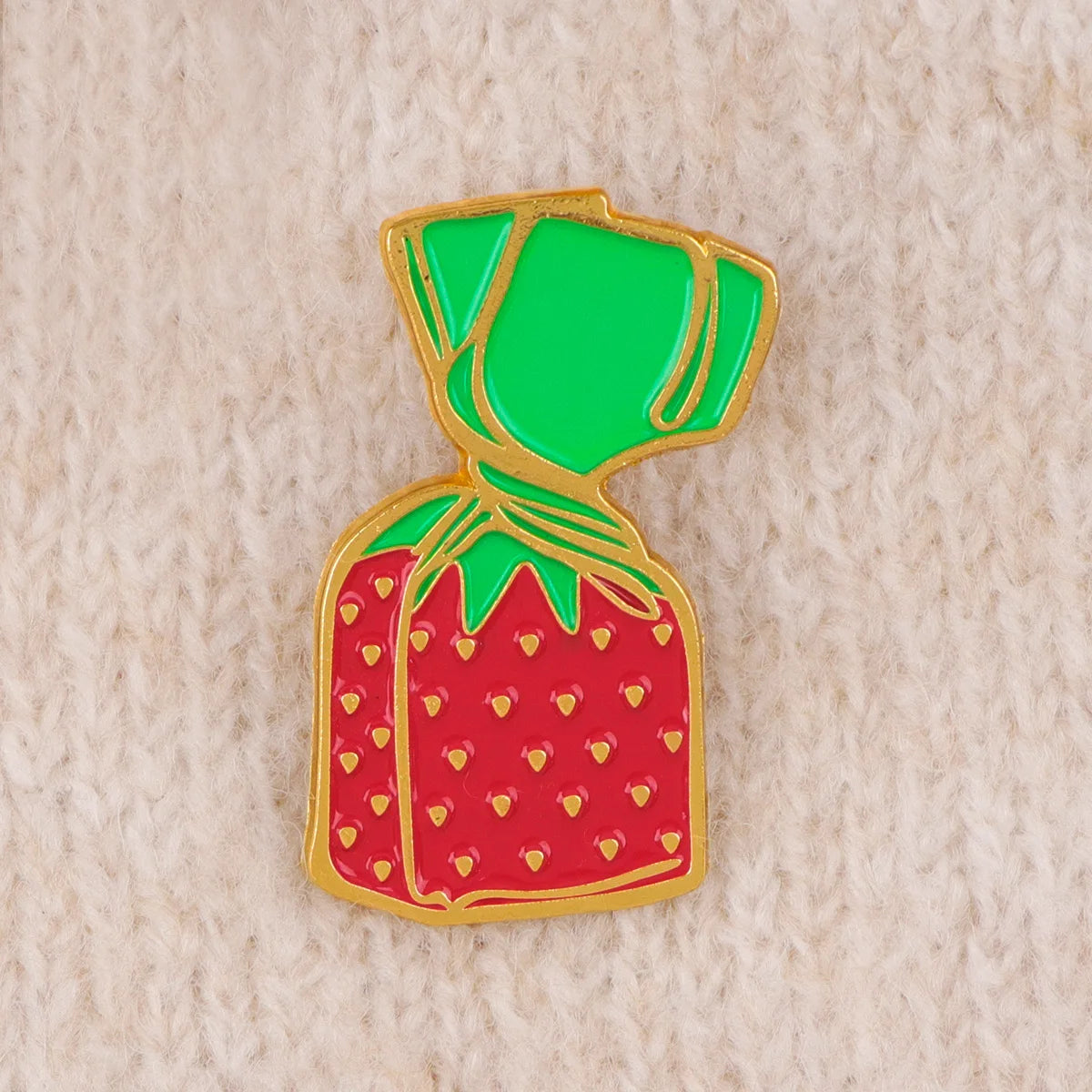 A shiny red strawberry enamel pin with a green stem and gold detailing.