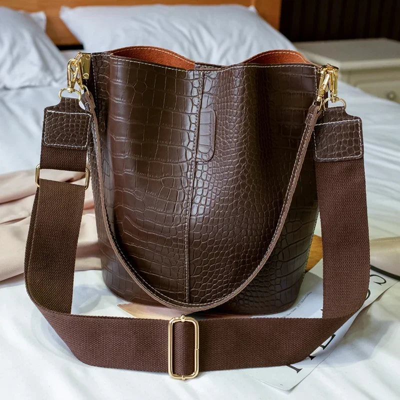 A brown vintage alligator pattern crossbody bag resting on white bedding.