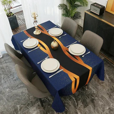 A dark blue geometric waterproof tablecloth set for a dining table with gold and white plates and a centerpiece.