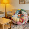 A large, colorful inflatable plush toy storage bag resting on a rug next to a wooden table.
