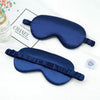 A dark blue silk sleep mask with a ruffled strap is displayed next to a Chanel box.