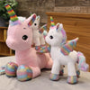 A pink unicorn plush toy with rainbow accents and a white unicorn standing beside it.