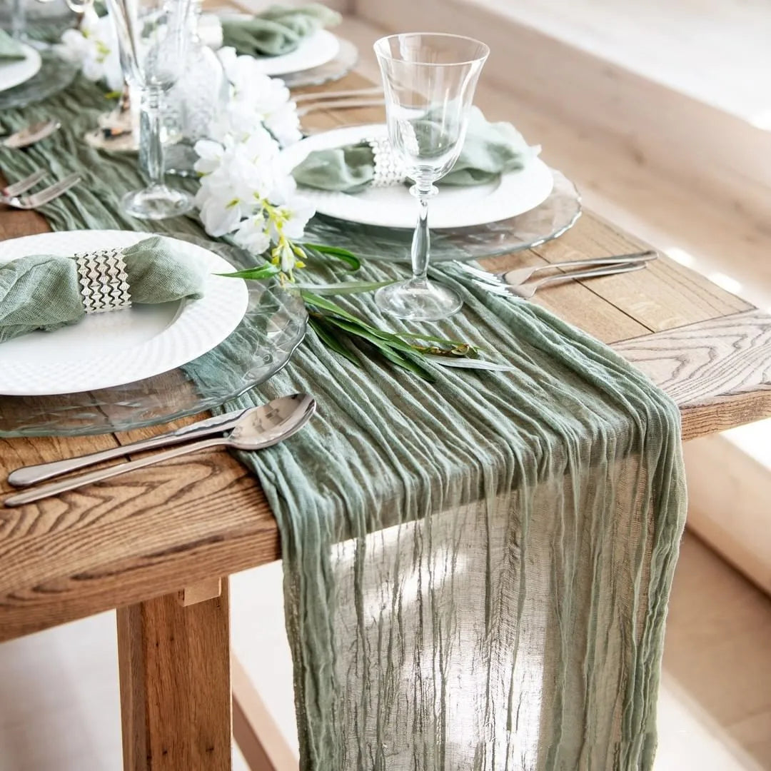 A rustic country boho table setting featuring a sage green cotton gauze table runner on a wooden table.