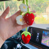 Hand holding a handmade crochet strawberry and flower pendant against a car mirror background