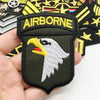 A close-up of a dark olive embroidered patch featuring a white eagle head and the word AIRBORNE on a hand.