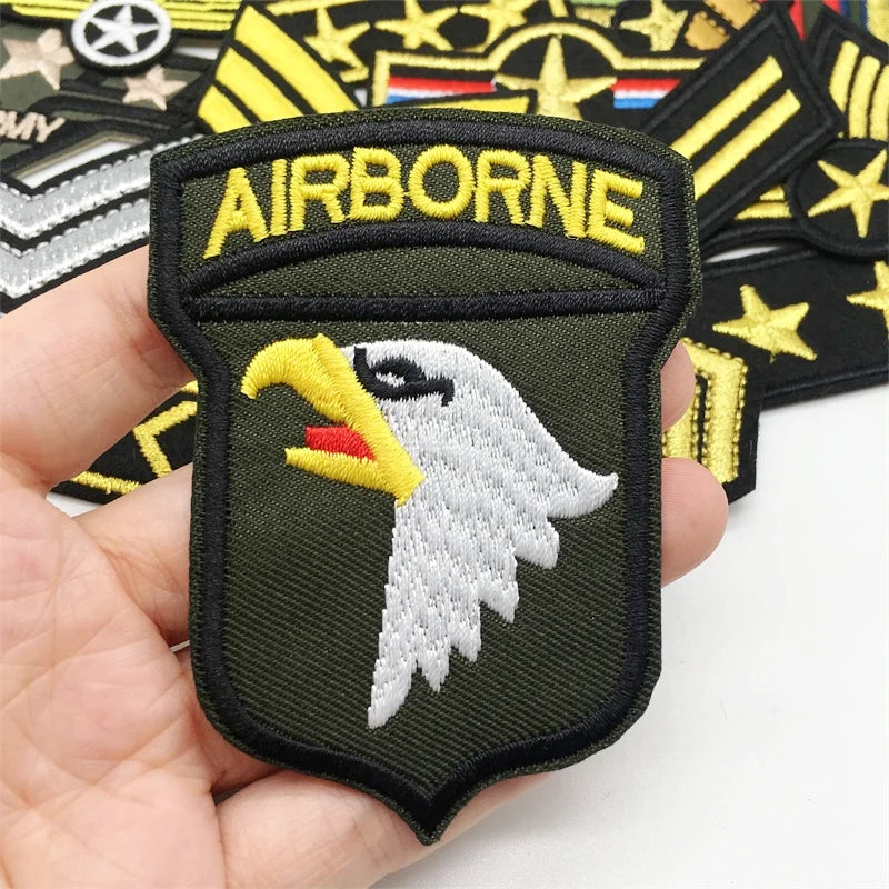 A close-up of a dark olive embroidered patch featuring a white eagle head and the word AIRBORNE on a hand.