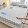 A white fitted mattress protector is shown on a bed, with a hand touching the fabric and water dripping onto it.
