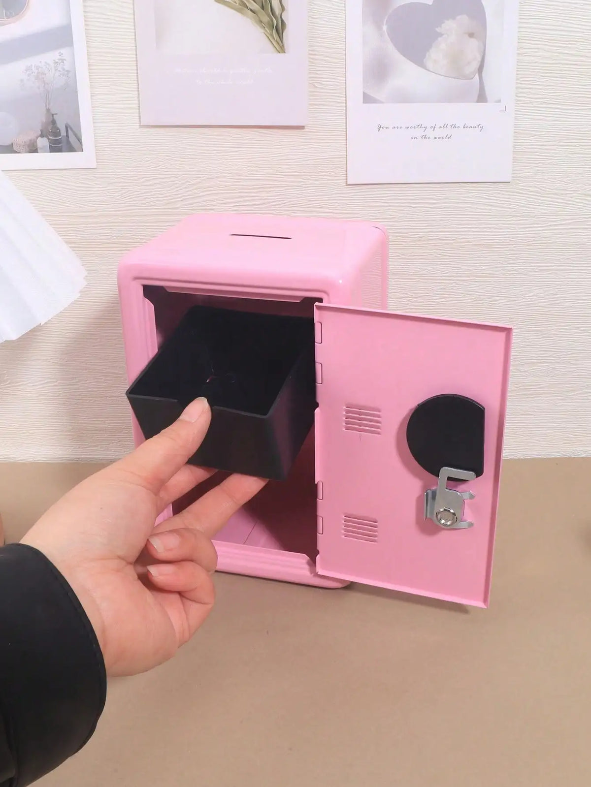 A hand opens a pink compact desktop safe with a combination lock, showing the interior compartment.