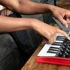 A person's hand is playing an AKAI Professional MPK Mini MK3 MIDI keyboard controller with drum pads and knobs on a wooden ta