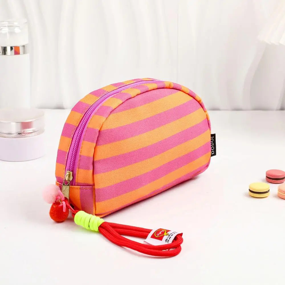 Pochette en crochet rayée rose et orange avec un cordon rouge, présentée sur une surface blanche.