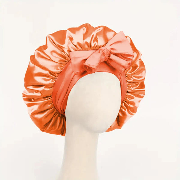 Orange satin sleep bonnet tied with a matching fabric bow displayed on a mannequin head.