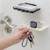 A hand is holding a set of keys and a small electronic device near a wall-mounted soap dish with drainage.