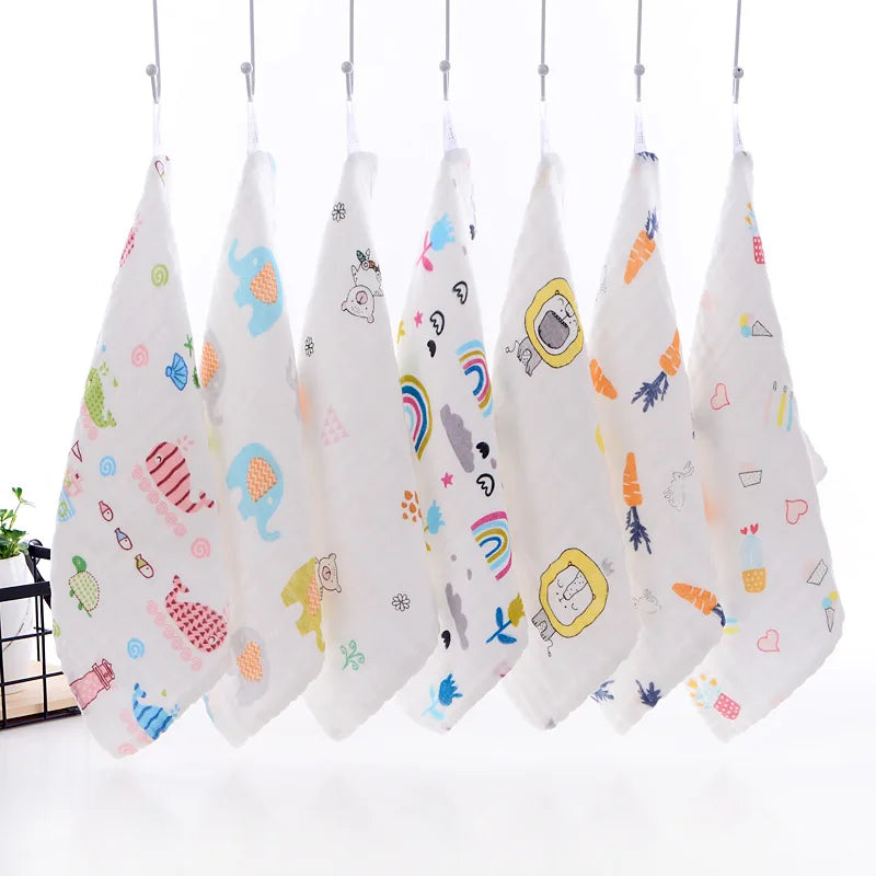 A set of five white muslin baby washcloths with colorful patterns hanging on a rack.